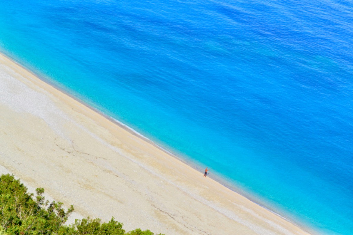An empty pale beach meeting turquoise water in a clean diagonal, seen from above